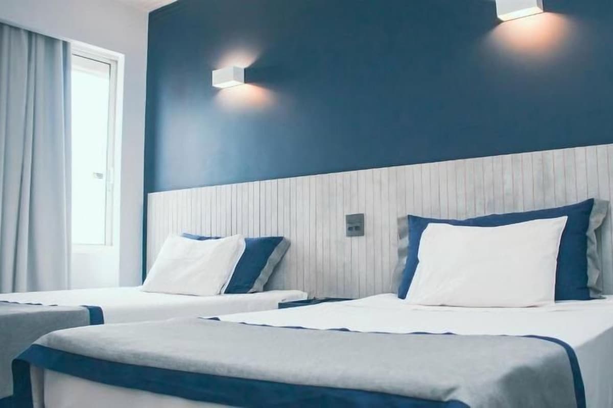 A hotel room with two beds, a window with curtains, and wall-mounted lighting.