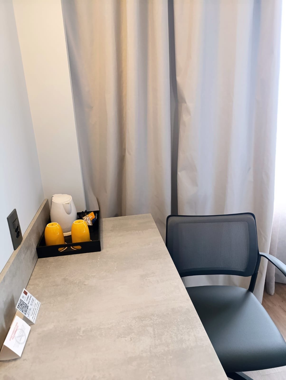 Quarto pequeno e moderno com uma mesa, uma cadeira, chaleira e um tabuleiro com xícaras e cafeteira.