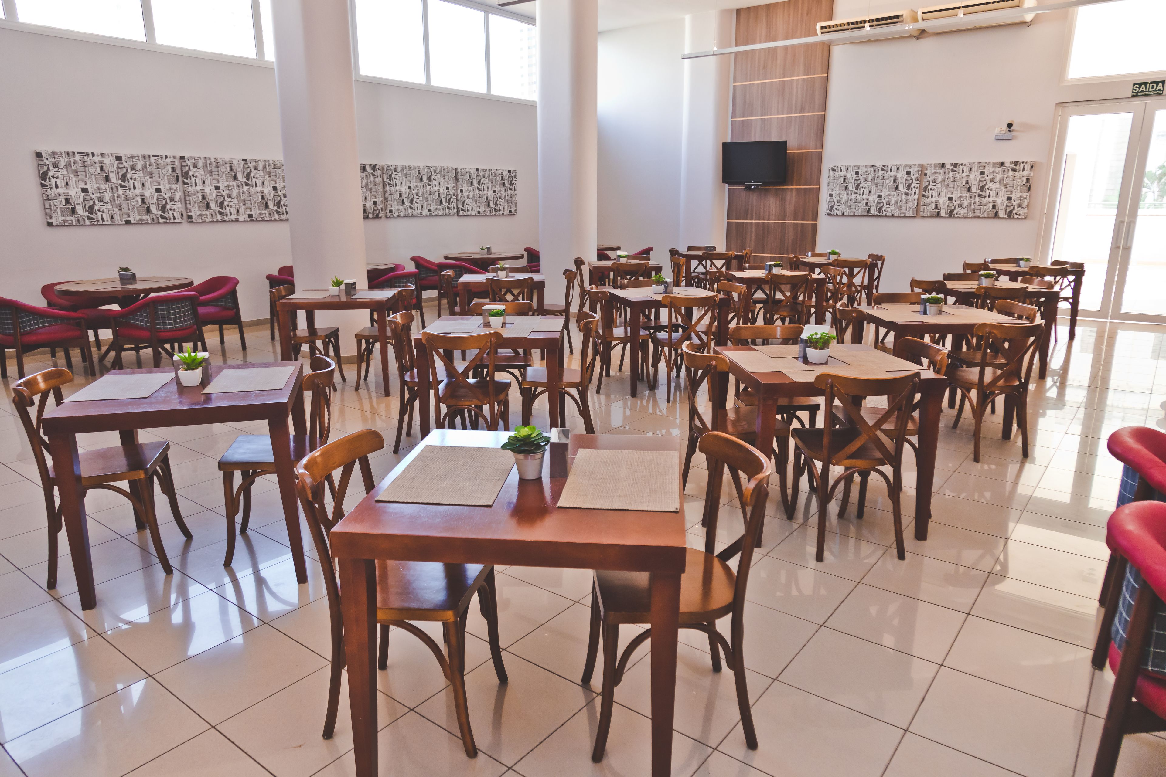 Un comedor amplio con múltiples mesas y sillas de madera, ventanas grandes y obras de arte en las paredes.