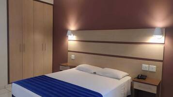 Una habitación de hotel con una cama, un armario, dos mesitas de noche y lámparas de pared.