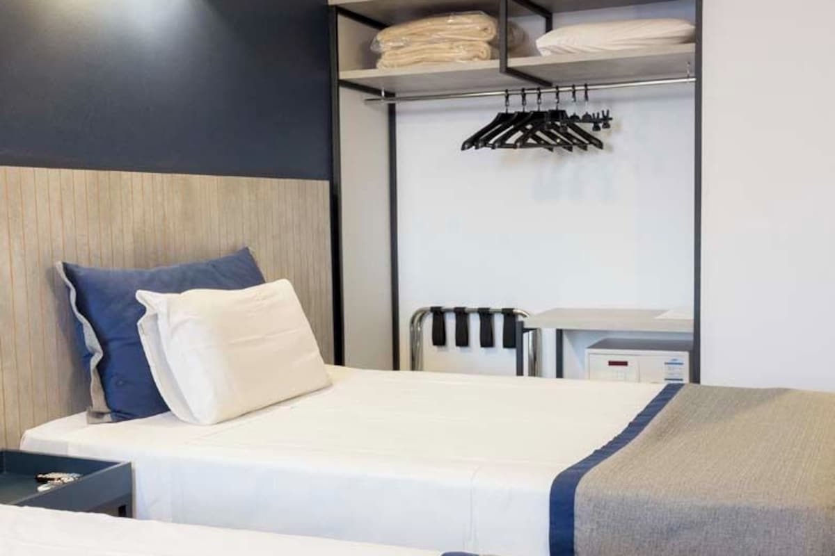 A hotel room with two beds, a wardrobe, a desk, and a hanging clothes rack.