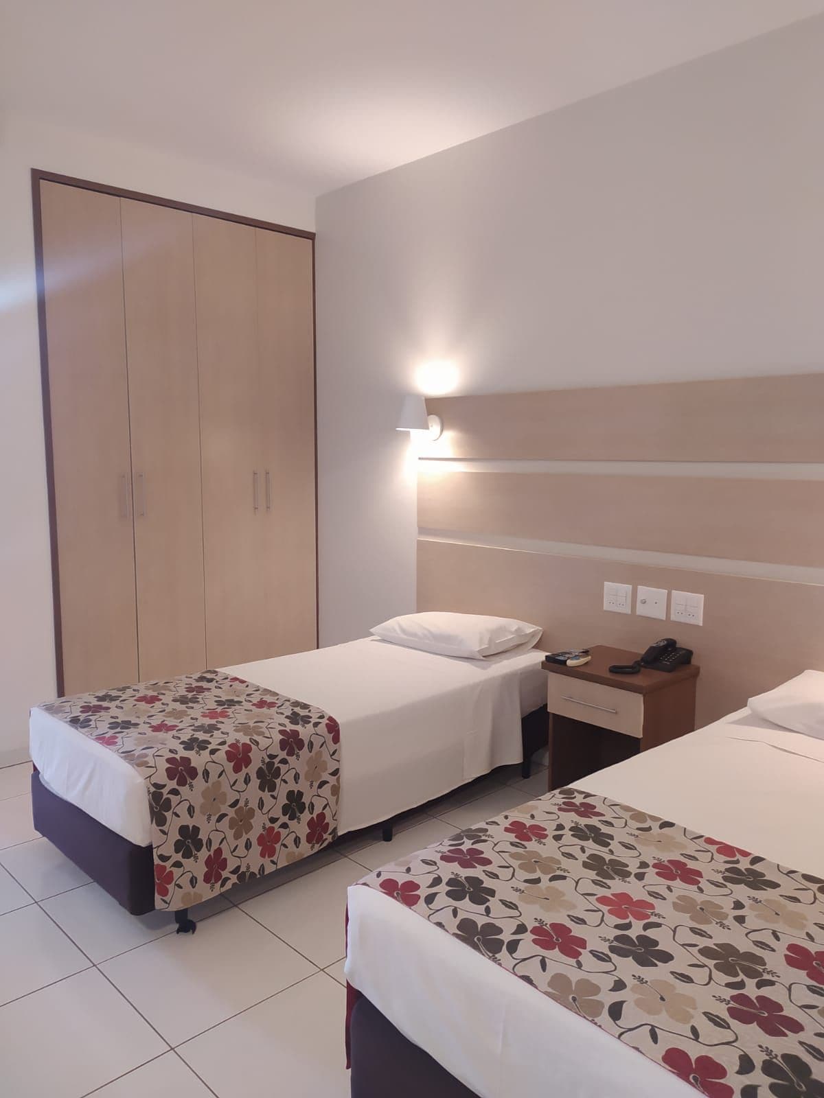 A hotel room with two single beds, a wardrobe, a bedside table with a lamp, and a phone.