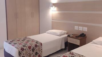 A hotel room with two single beds, a wardrobe, a bedside table with a lamp, and a phone.