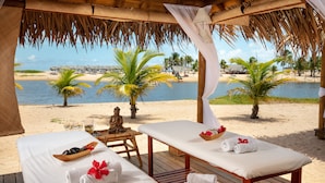 Un spa frente al mar con mesas de masaje de madera, toallas y una estatua de Buda.