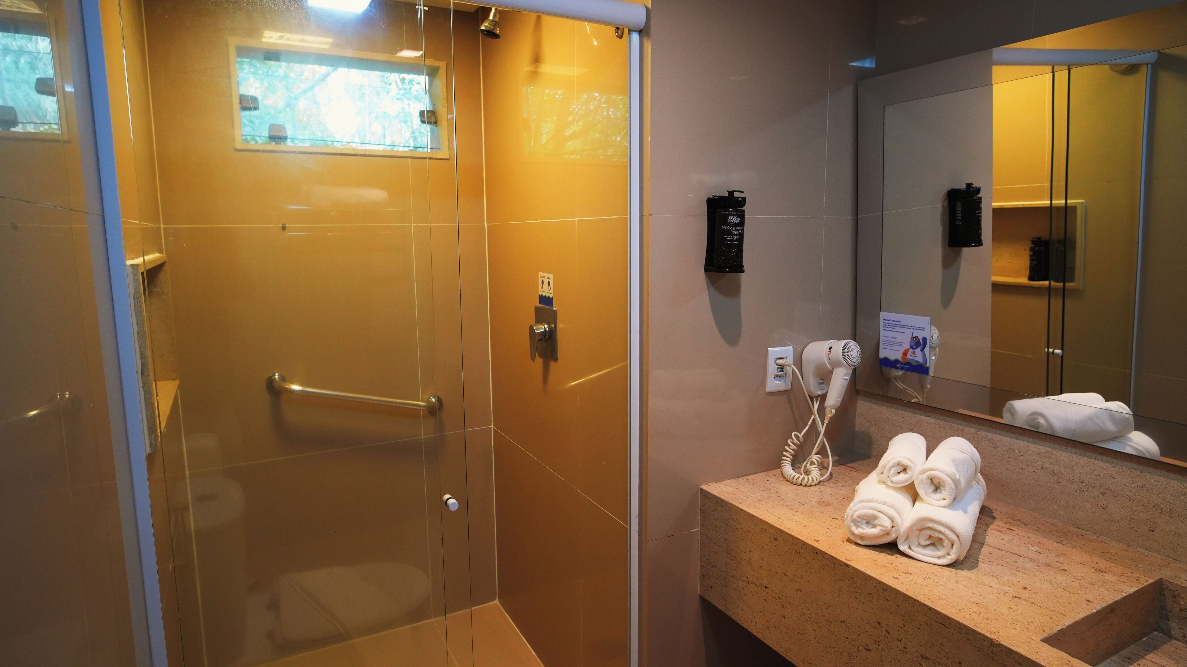 A bathroom with a glass shower enclosure, a towel rack, a hairdryer, and a mirror reflecting a towel.