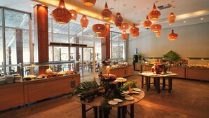 Un amplio vestíbulo de hotel con techos altos, ventanas grandes y una zona de buffet.