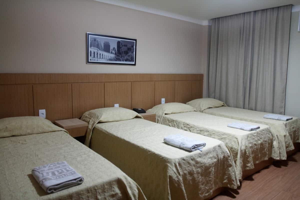 A hotel room with three single beds, a wooden headboard, a framed picture on the wall, and a large window with curtains.