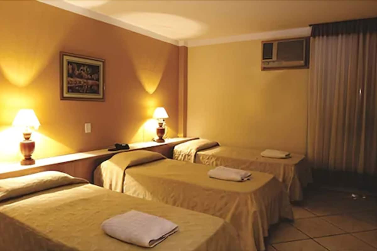 A hotel room with two single beds, each with a bedside table and lamp, a small window, and a painting on the wall.