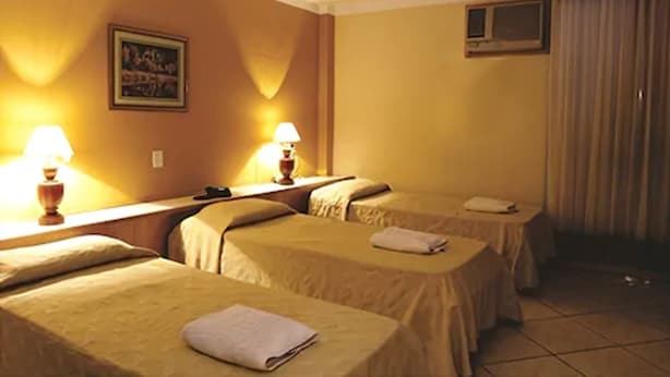 Habitación de hotel con dos camas individuales, cada una con mesita de noche y lámpara, un ventanal pequeño y un cuadro en la pared.