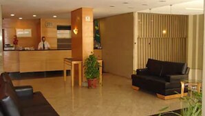 Un vestíbulo de hotel con una mesa de recepción, un sofá de cuero negro y una planta en maceta.