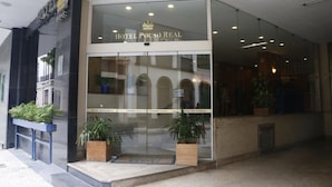 El exterior del Hotel Pouso Real, con fachada de vidrio, un logo de corona sobre la entrada y plantas en macetas a la entrada.