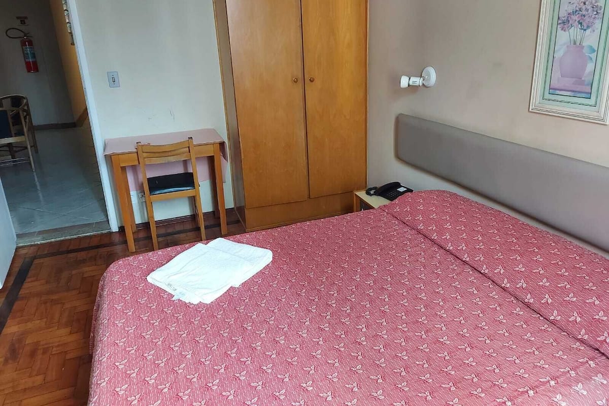 A bedroom with a bed, a wooden wardrobe, a desk, and a chair.