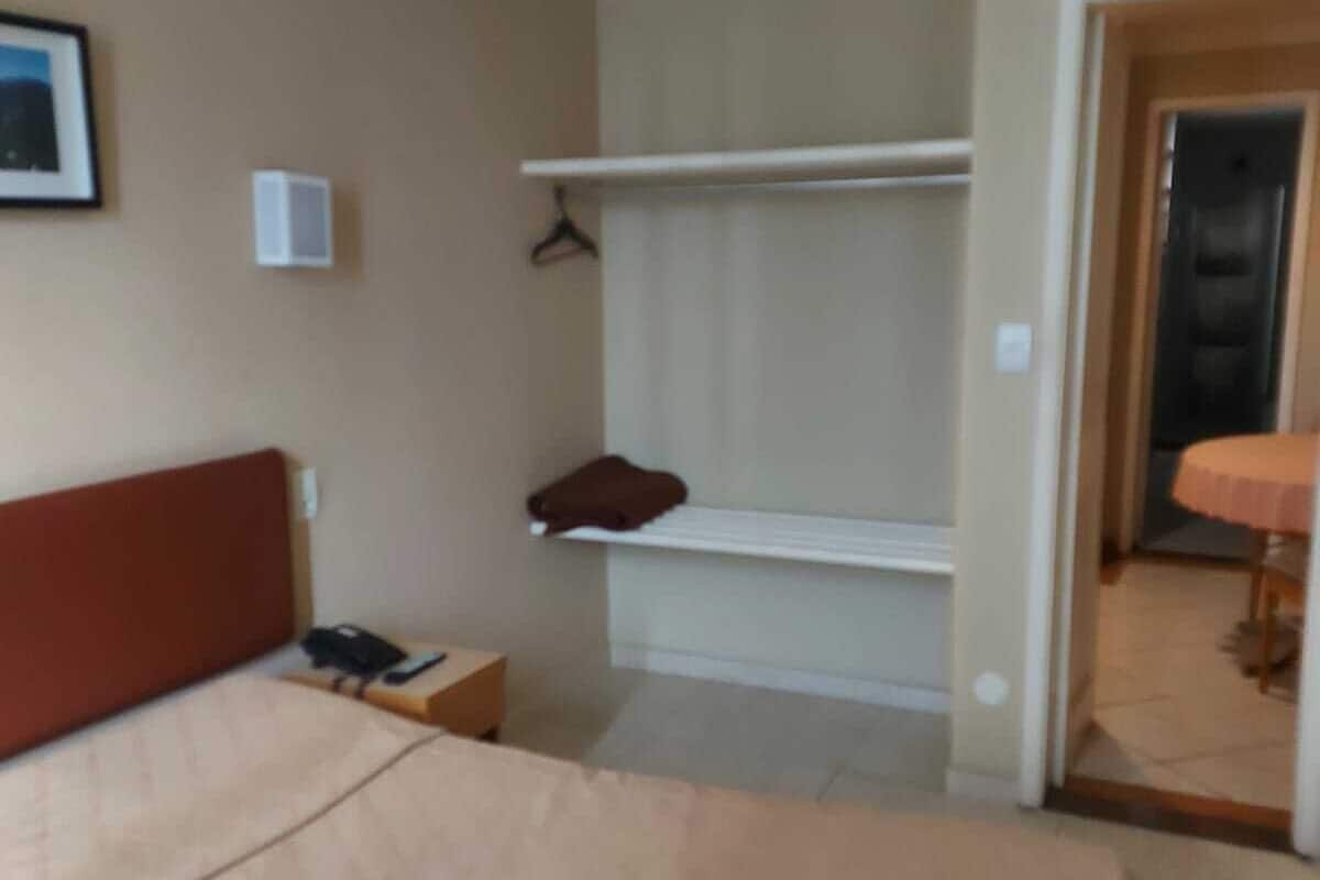 A hotel room with a bed, a bedside table, a coat rack, and a door leading to another room.