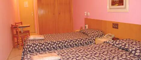 Una habitación con dos camas, un armario de madera, un escritorio con una silla y un cuadro en la pared.
