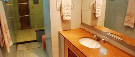 Un baño con tocador de madera, lavamanos, espejo y zona de ducha.