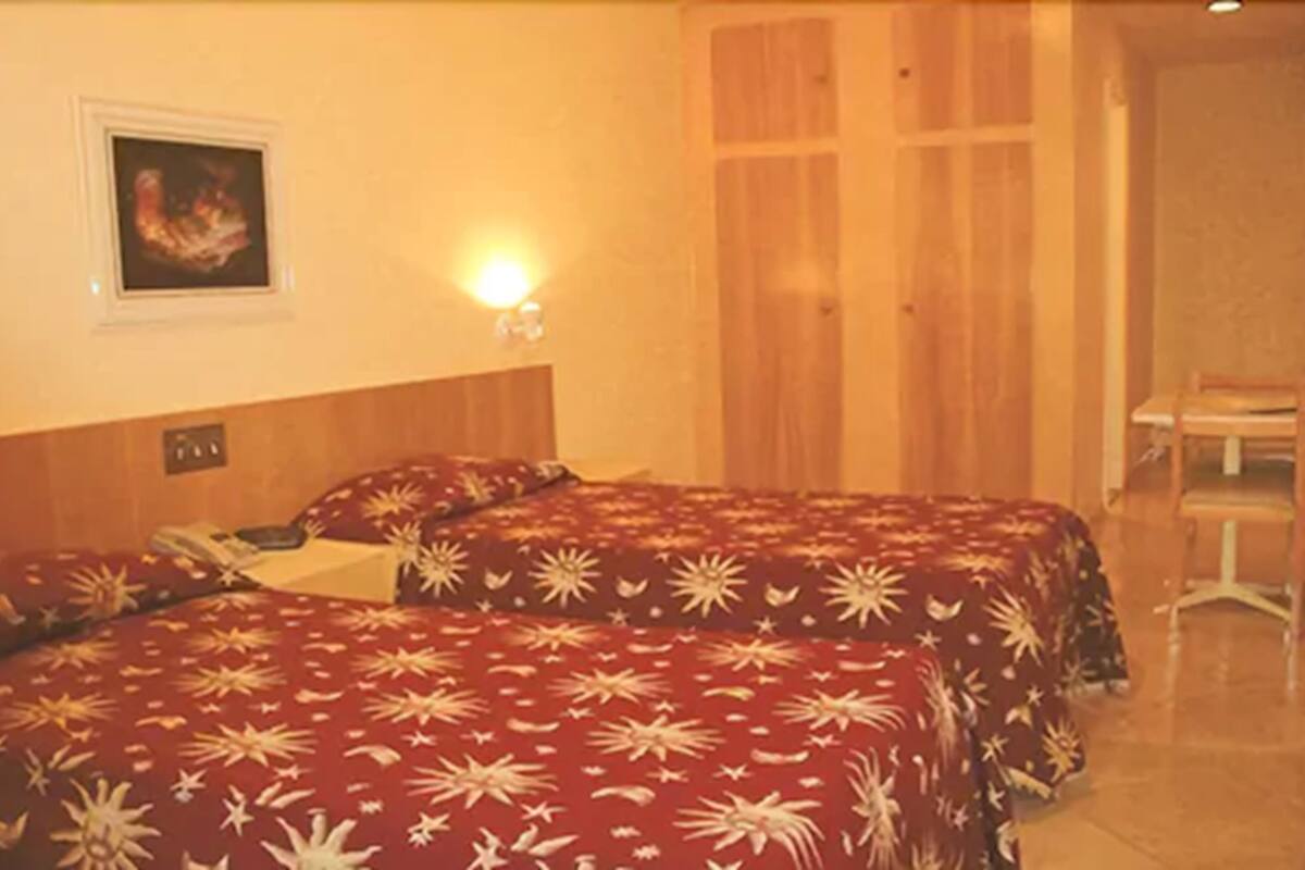A hotel room with two beds, a wooden headboard, a wall-mounted light, and a door with a wooden panel.