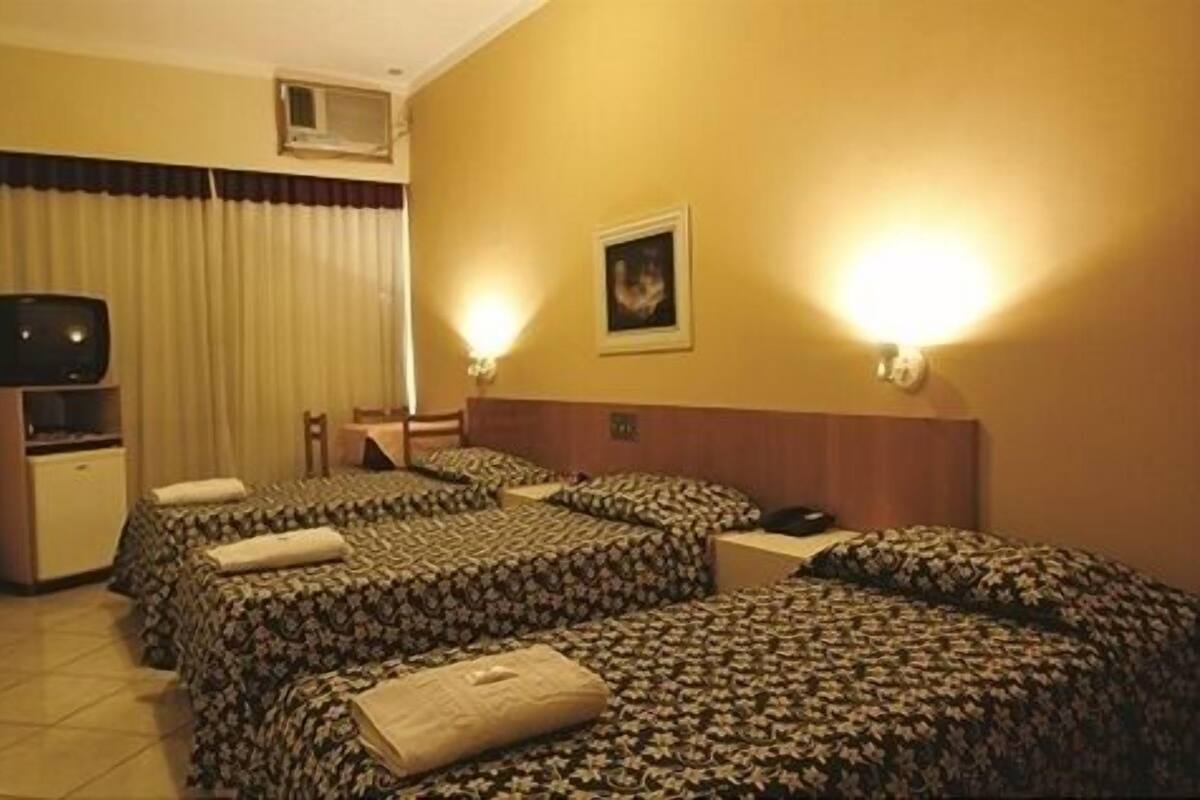 A hotel room with two beds, a television, a desk, and a wall-mounted air conditioner.