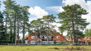 A large brick house with multiple chimneys, surrounded by a grassy field and tall trees. - Beaulieu Hotel (Brockenhurst)