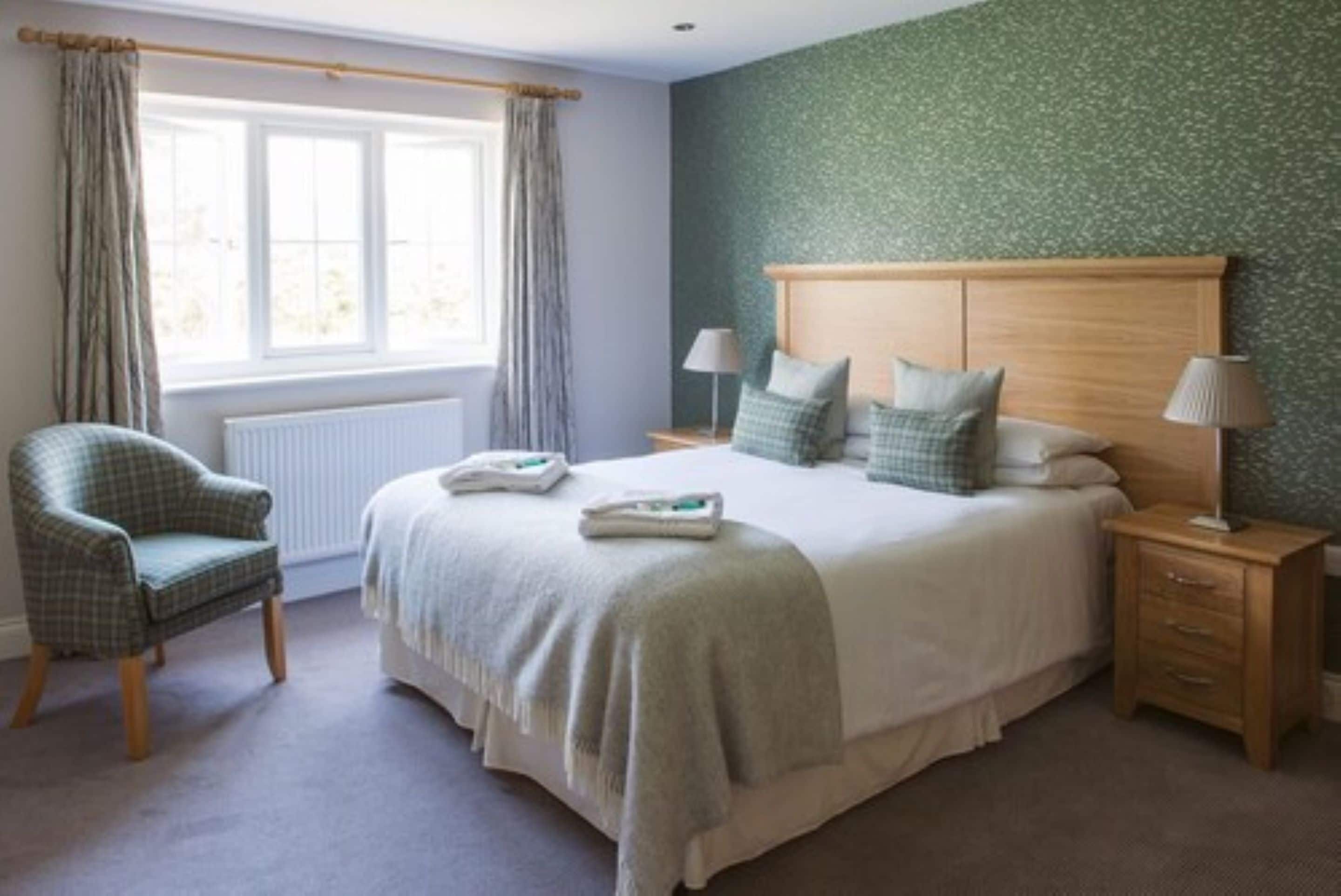 A bedroom with a large bed, two bedside tables, a chair, and a window with curtains.