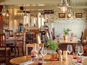 A restaurant with wooden tables, chairs, and hanging light fixtures. - Beaulieu Hotel (Brockenhurst)
