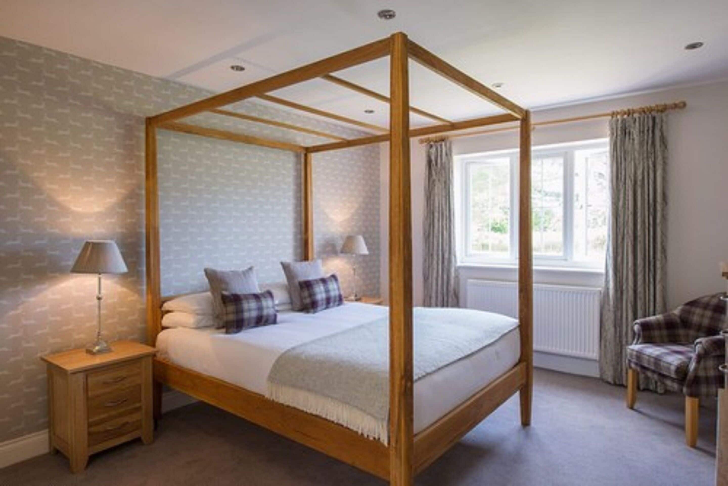A four-poster bed in a bedroom with a nightstand, a lamp, and a chair.