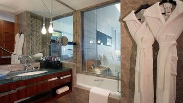 Un baño moderno con un lavabo de vidrio, un espejo grande y una bañera.
