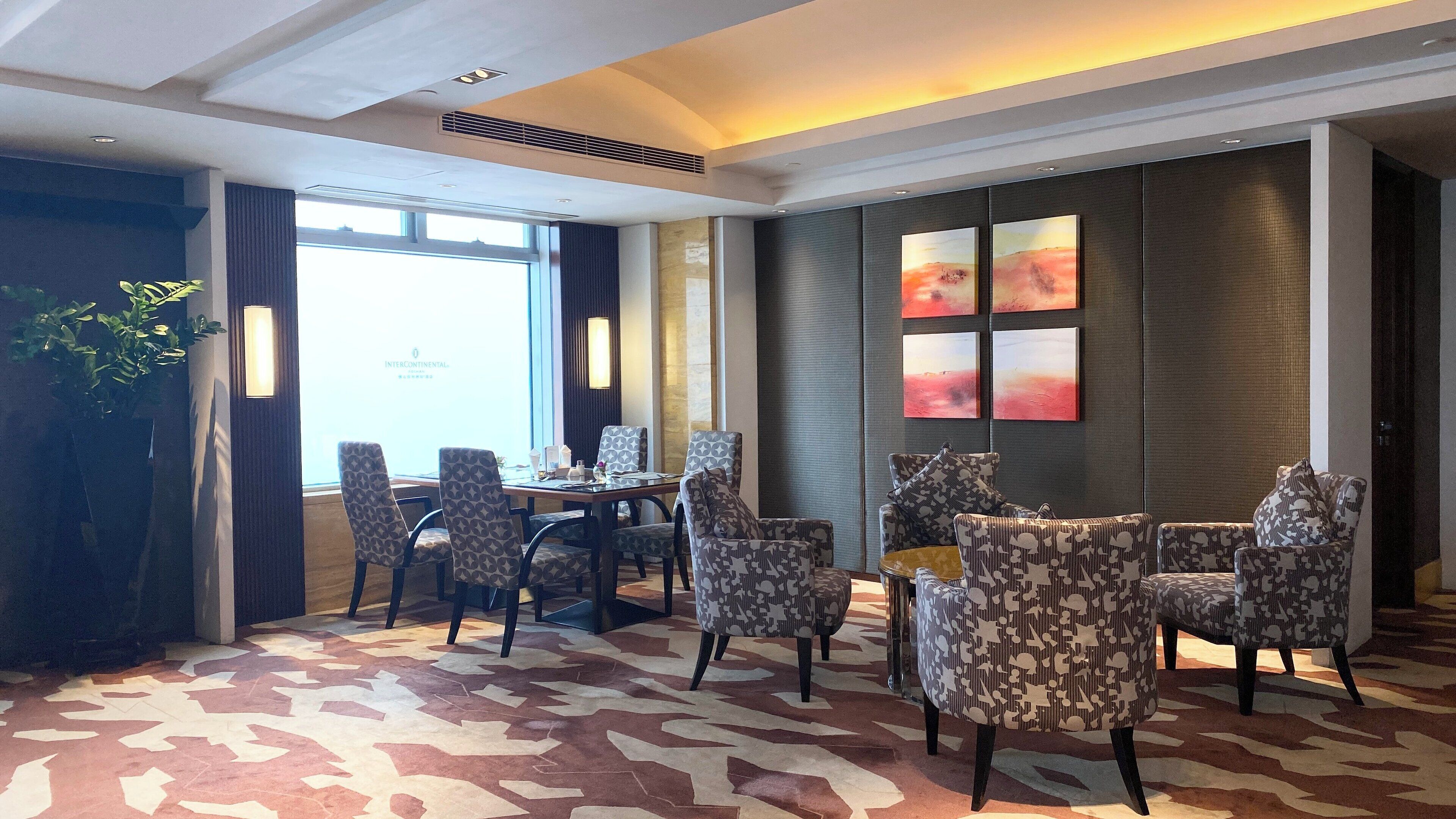 Un comedor de hotel con una gran mesa y sillas, alfombra estampada y obras de arte en las paredes.
