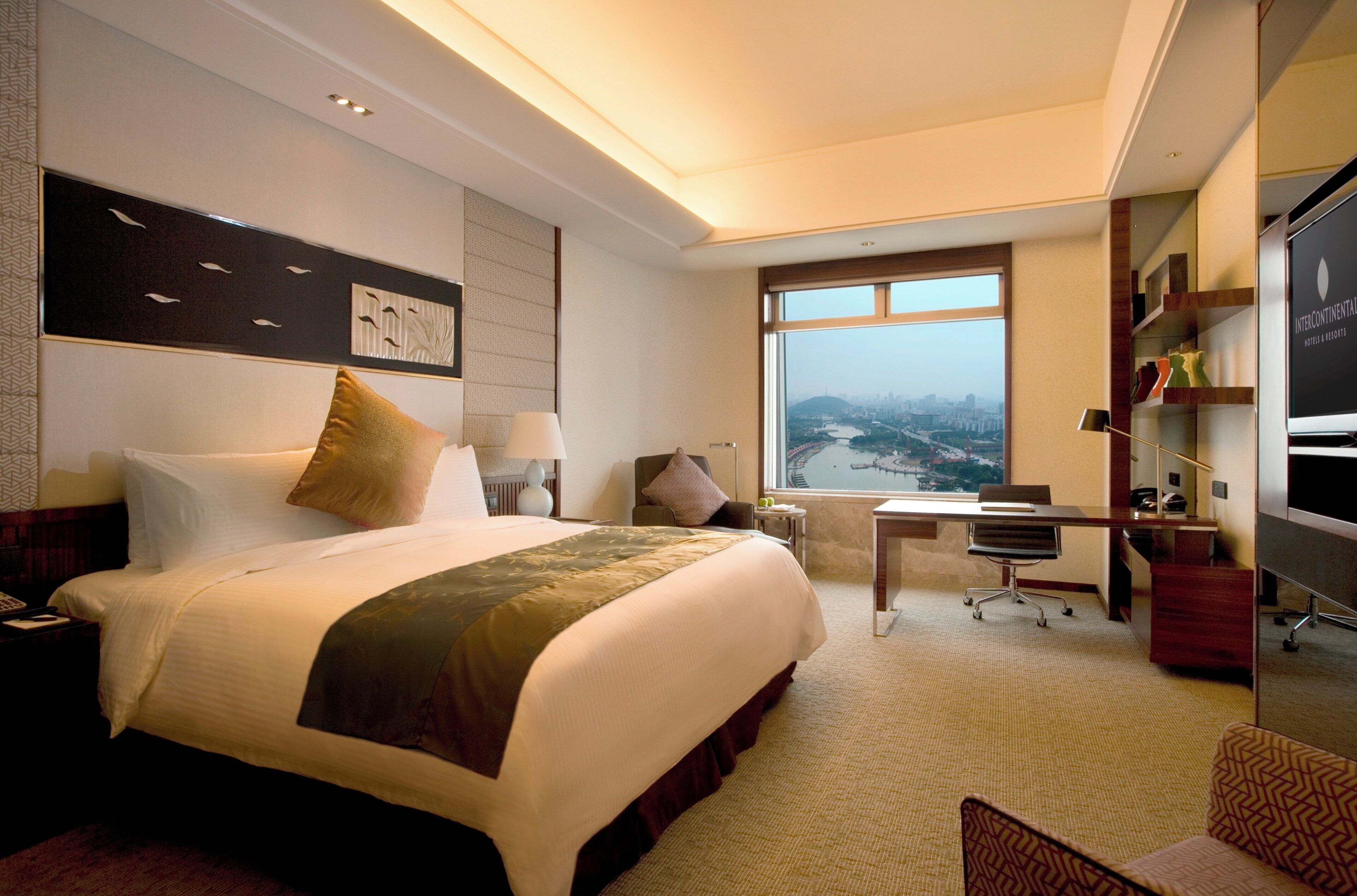 A hotel room with a large bed, a desk, a chair, and a TV.