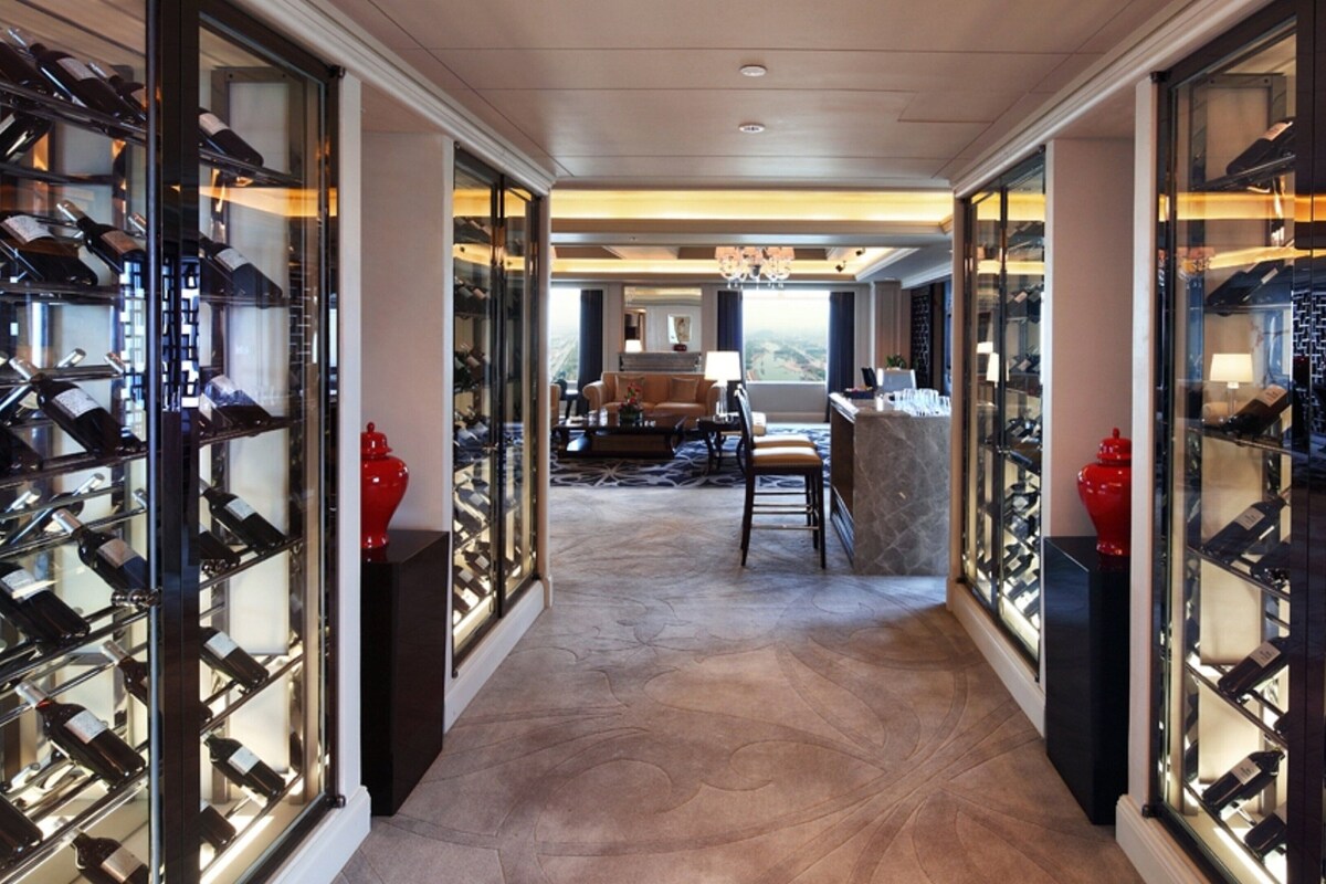A wine cellar with rows of wine racks, a seating area with a sofa and chairs, and a view through the glass doors.