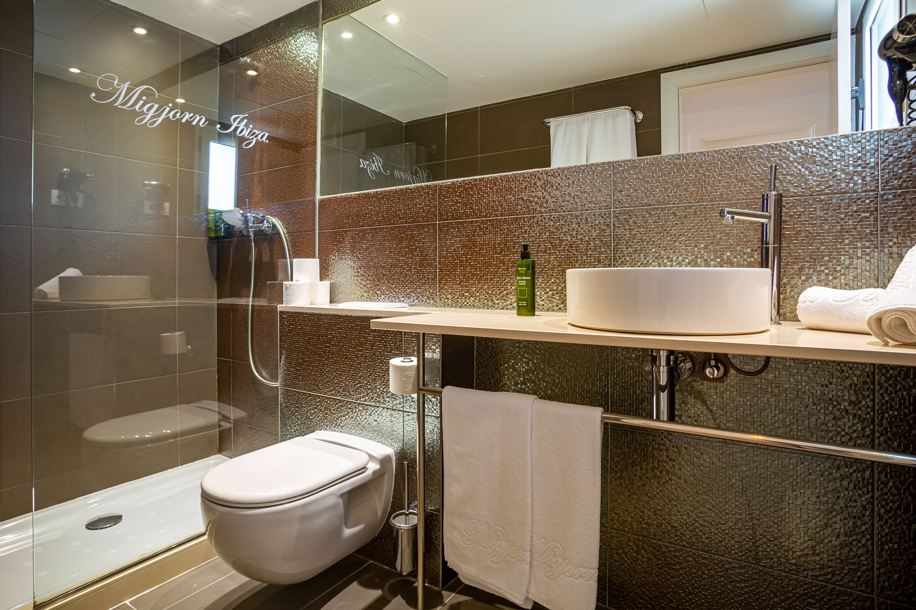 Un baño moderno con cabina de ducha de vidrio, inodoro blanco y tocador con lavabo y perchero para toallas.