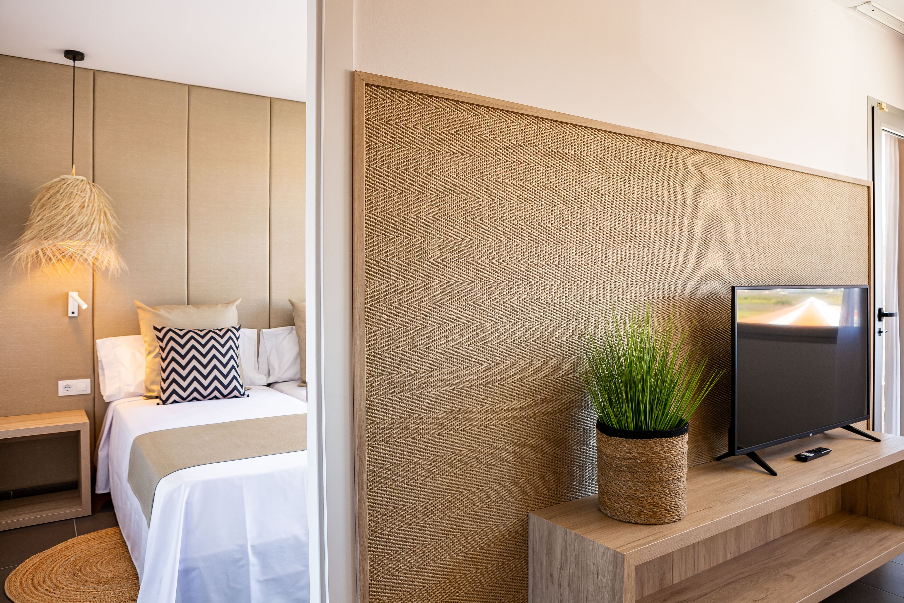 Ein modernes Hotelzimmer mit Bett, Nachttisch, Lampe, Fernseher und einer dekorativen Wandverkleidung.