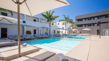 Un área de piscina con sillones de descanso y sombrillas, una piscina azul cristalina y palmeras.