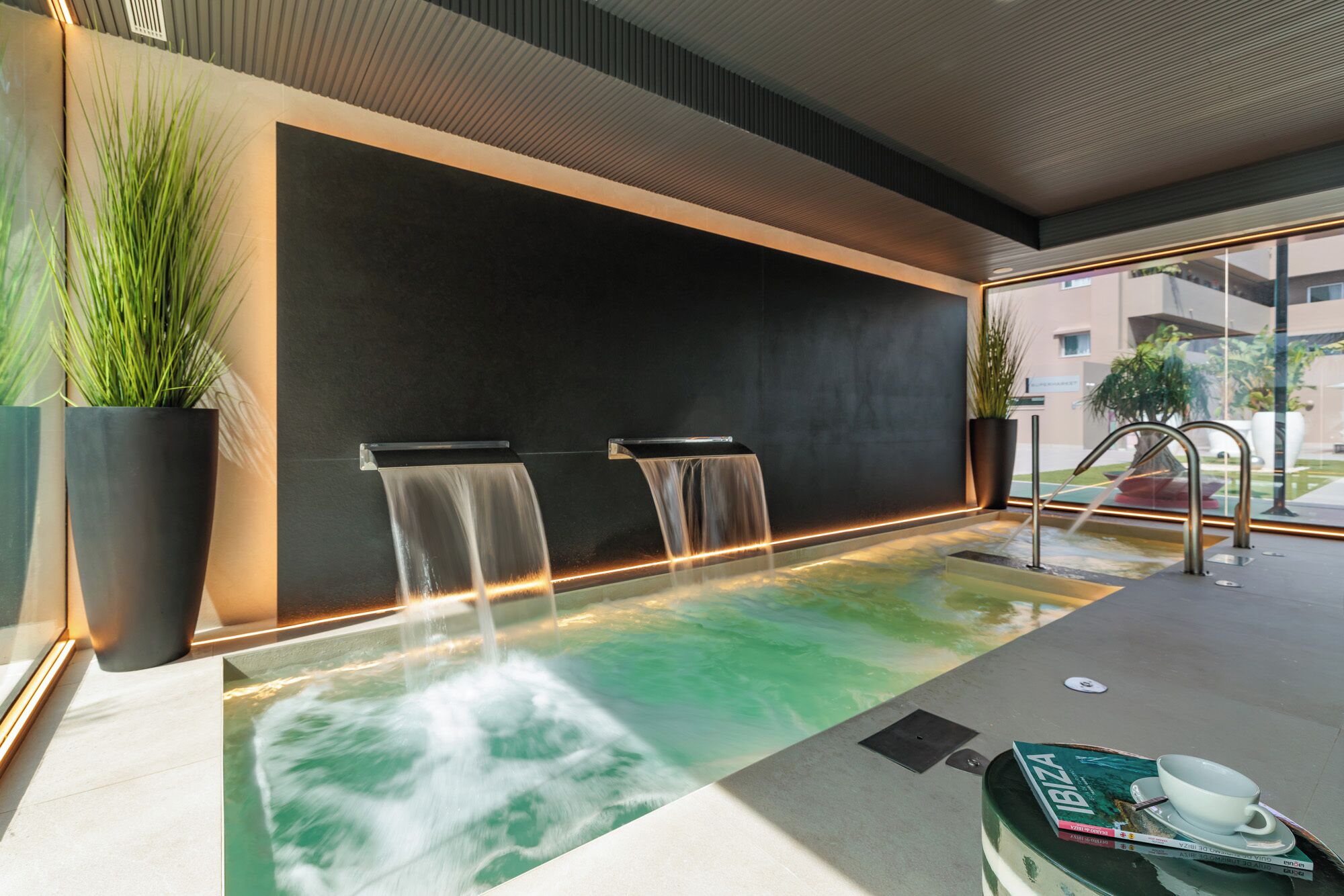 Un espace spa doté d’un plancher chauffant, de deux cascades et d’un coin salon avec un livre et une tasse.