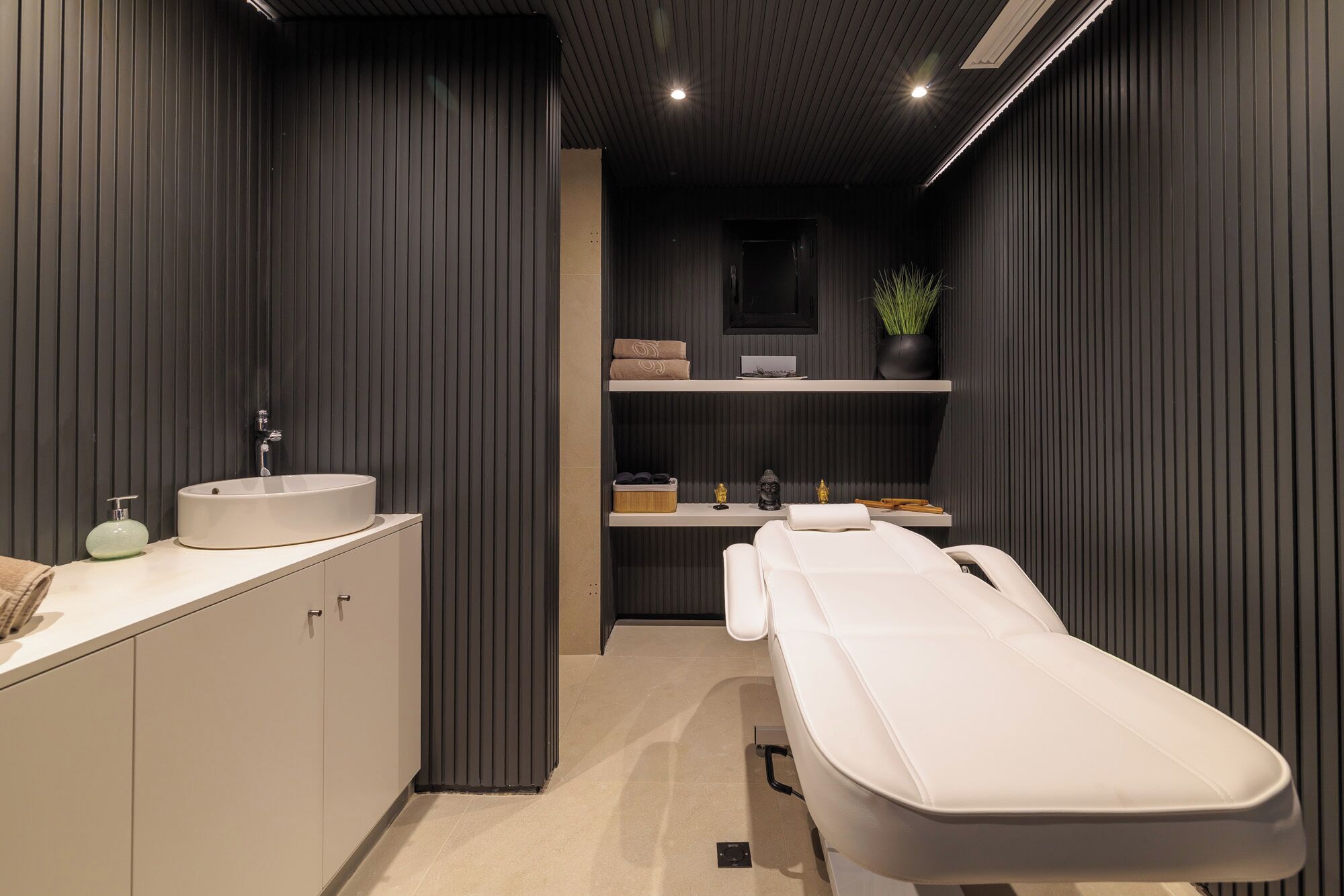 A modern bathroom with a white sink, a mirror, a towel rack, and a massage table.