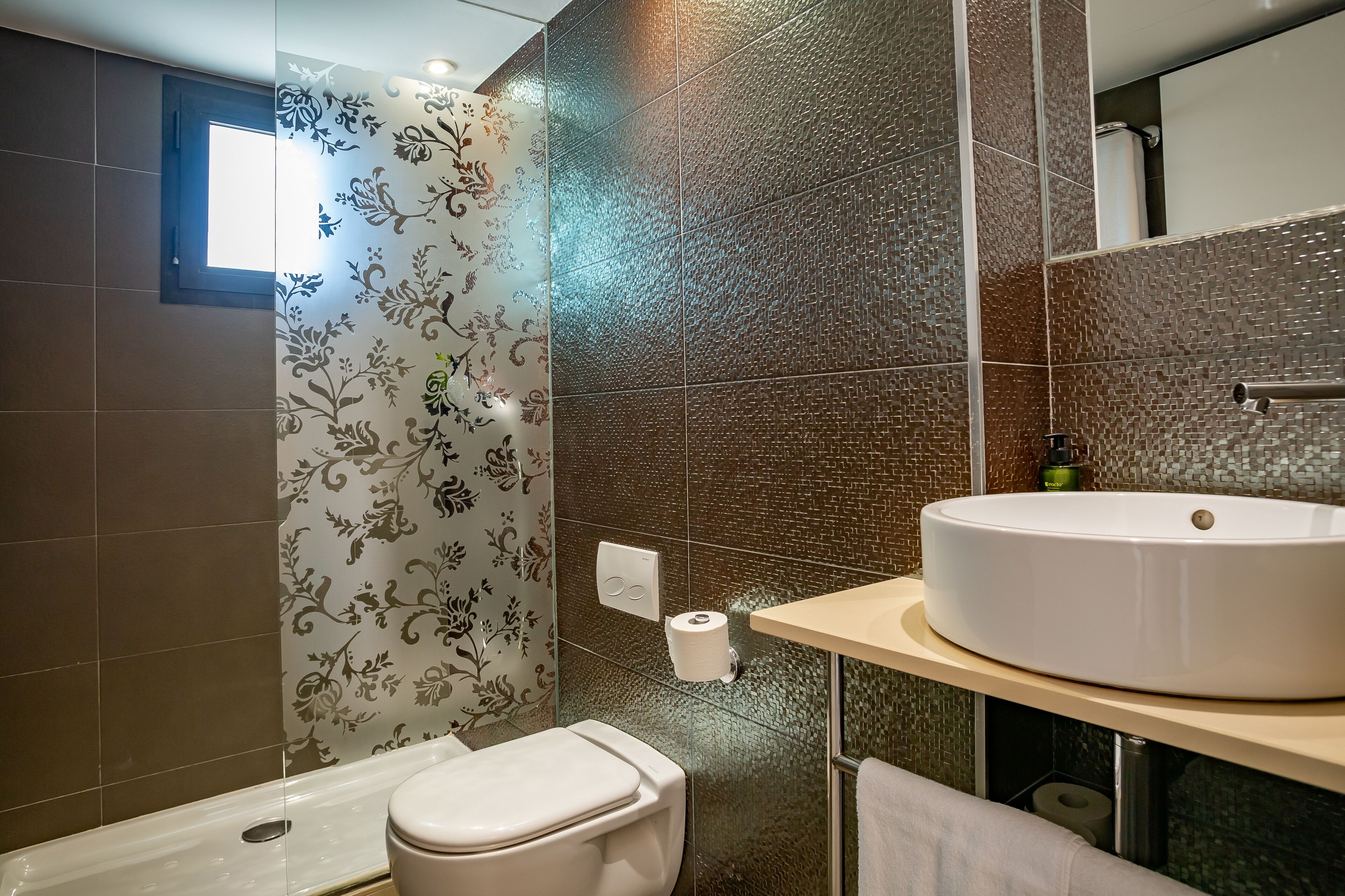 A modern bathroom with a toilet, a large sink, and a shower area.