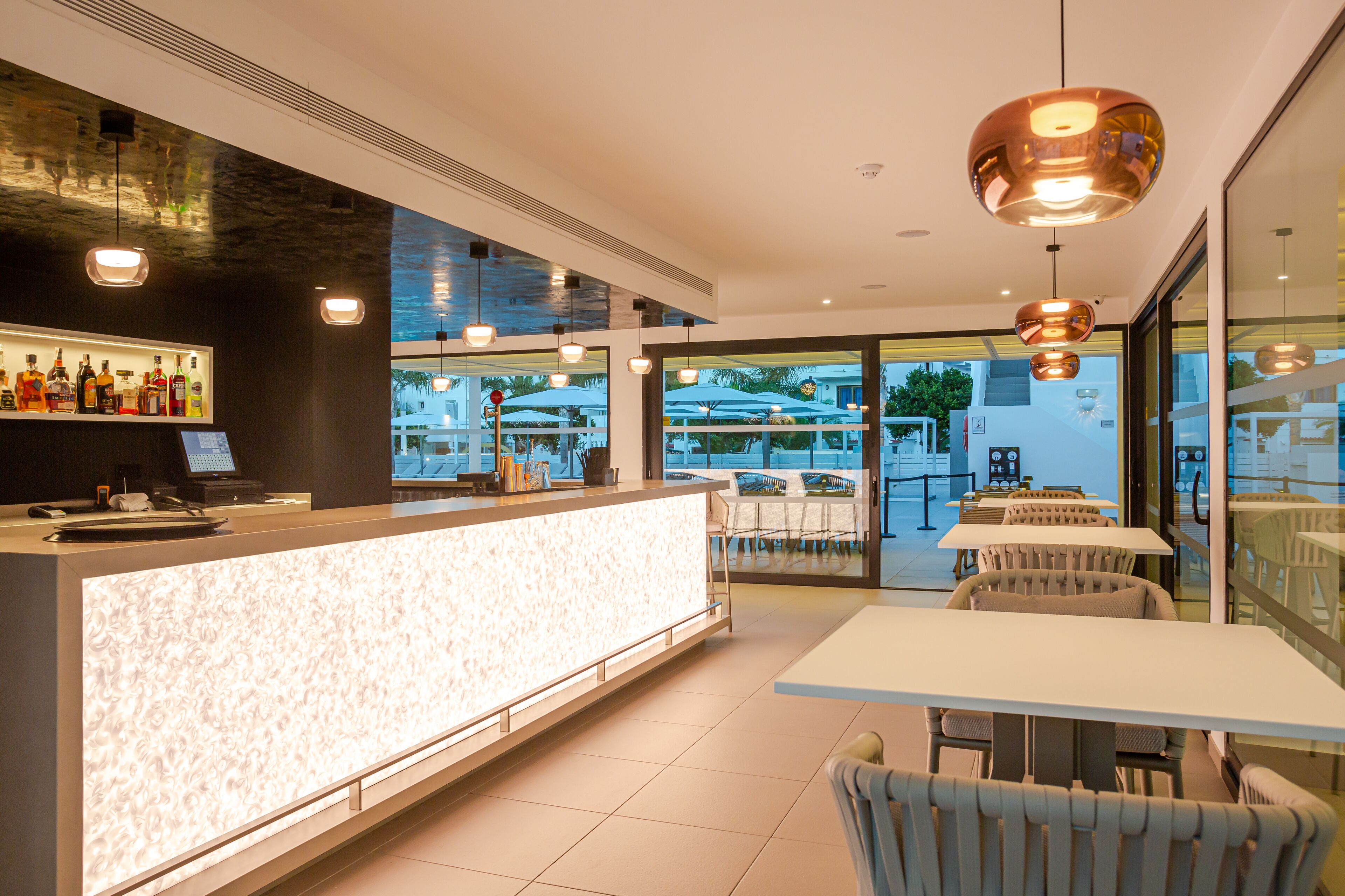 Un moderno vestíbulo de hotel con una recepción, área de descanso y grandes ventanales que ofrecen vistas del patio exterior.