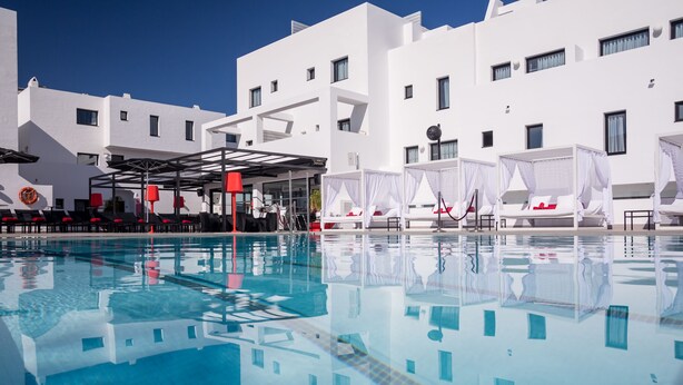 A swimming pool with clear blue water, white buildings, and red chairs. - Migjorn Ibiza Suites & Spa (Sant Josep de sa Talaia)
