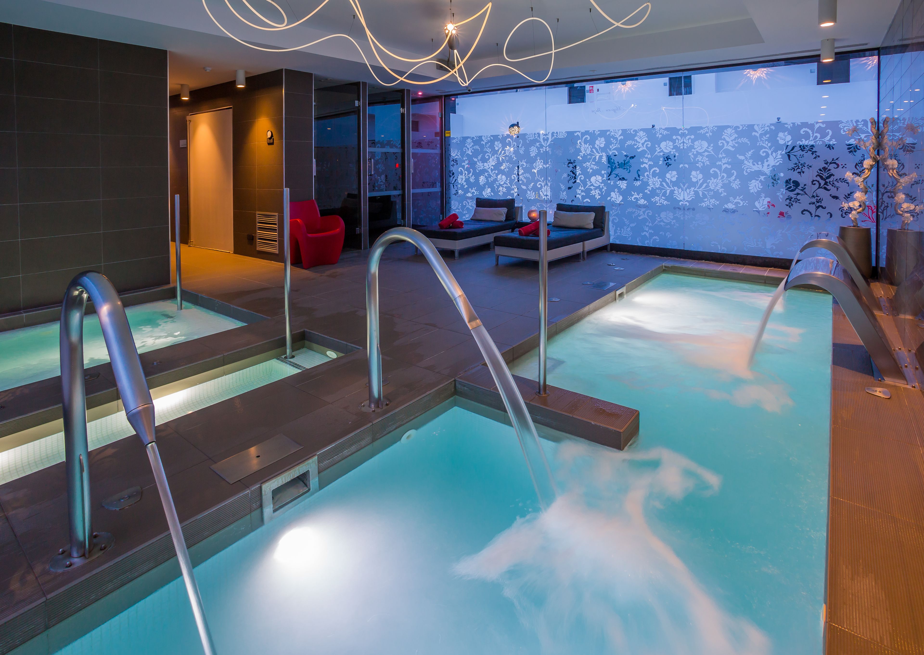 Une piscine intérieure moderne dotée de plusieurs bains à remous et d’espaces de détente.