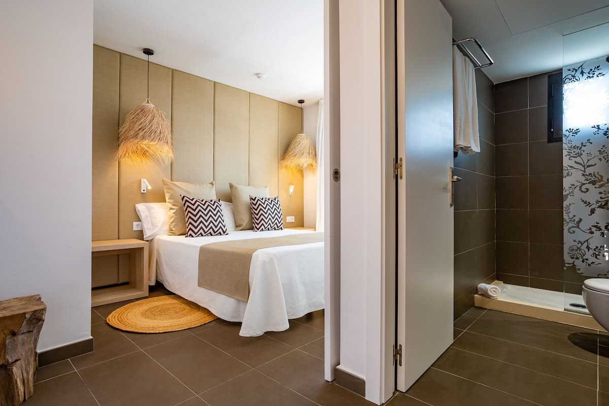 A modern bedroom with a bed, bedside lamps, and a view into a bathroom with a shower and toilet.