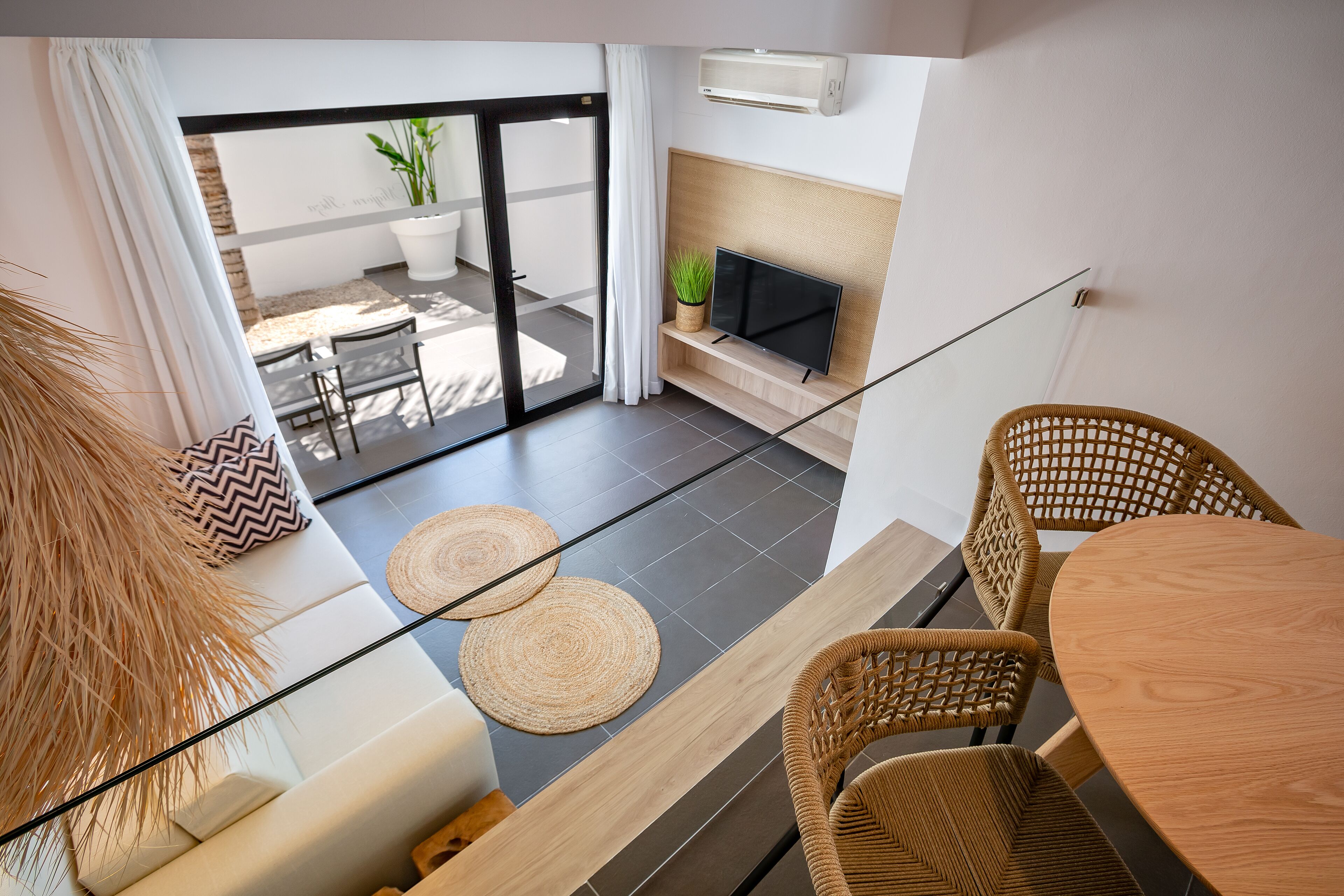 A modern living room with a glass door leading to a balcony, a flat-screen TV, wicker furniture, and a potted plant.