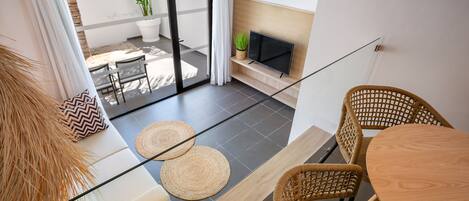A modern living room with a glass door leading to a balcony, a flat-screen TV, wicker furniture, and a potted plant.
