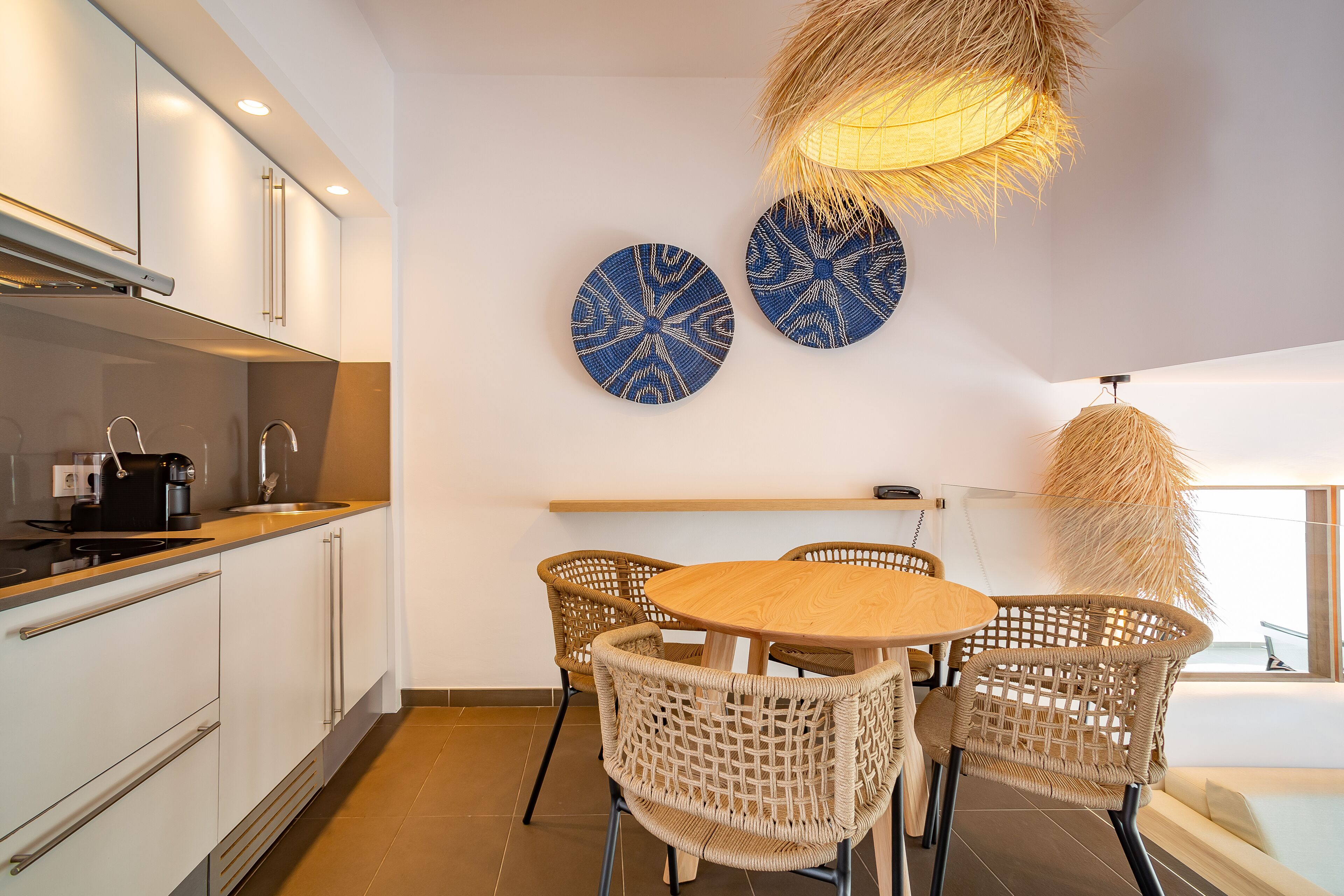 Una cocina moderna con armarios blancos, una mesa de comedor de madera, sillas de mimbre y platos decorativos azules en la pared.