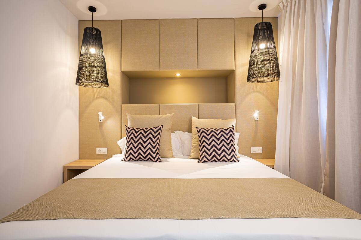 A hotel room with a large bed, two bedside lamps, a headboard with storage, and a nightstand.