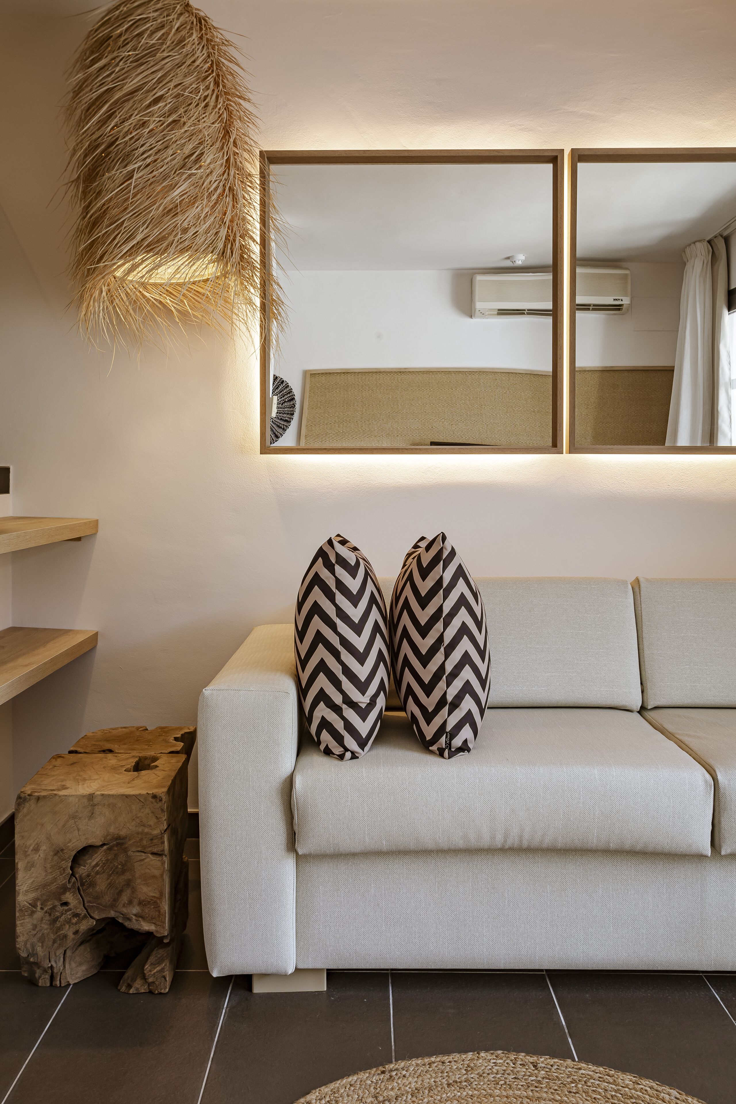 Una sala de estar moderna con un sofá, dos almohadones estampados, un taburete de madera y una lámpara colgante.
