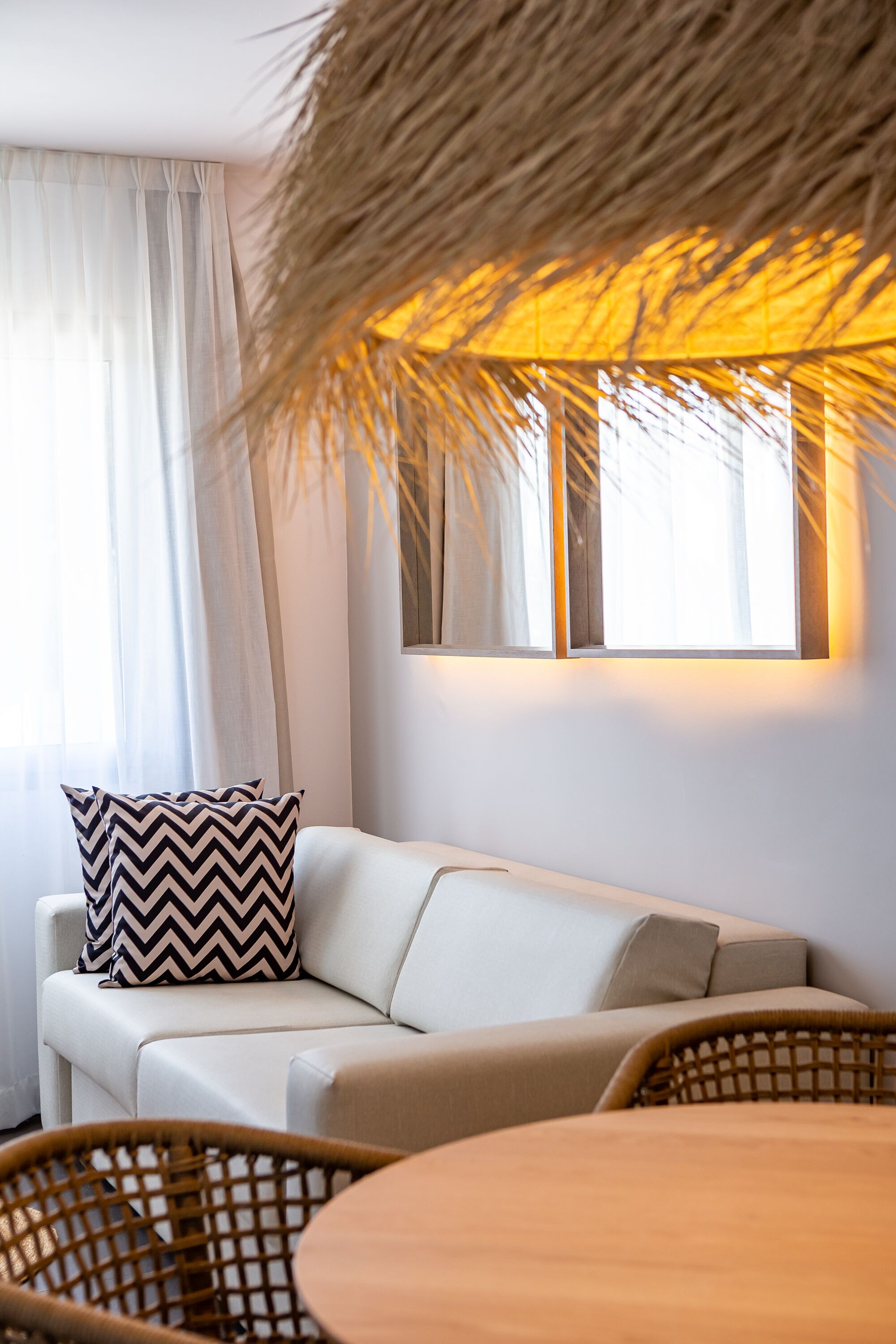 Una sala moderna con un sofá, un cojín estampado, una silla de fibras naturales y una mesa.