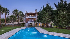 A modern two-story house with a swimming pool, surrounded by palm trees and a stone wall. - Athina Luxury Villas (Platanias)