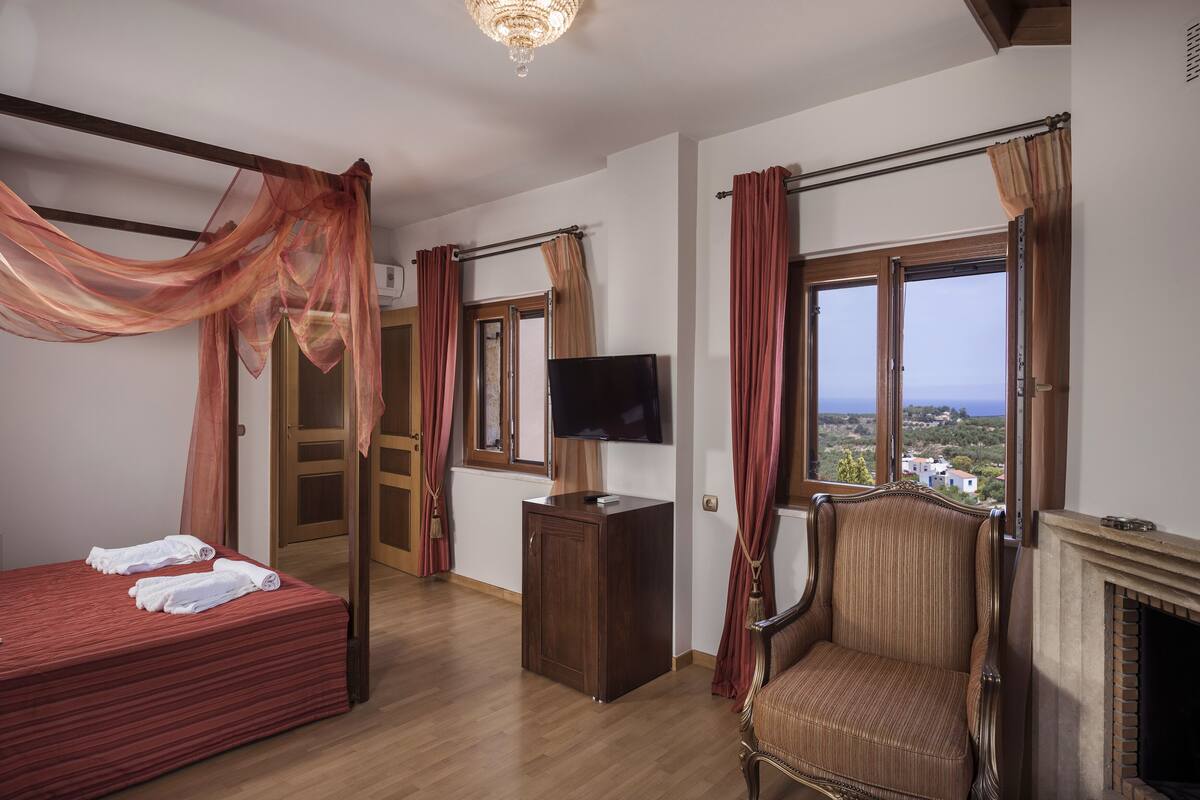 Een slaapkamer met een bed, een televisie, een stoel, een open haard en uitzicht op het landschap.