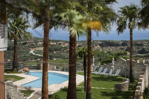Una piscina rodeada de palmeras, un muro de piedra y vistas al paisaje.
