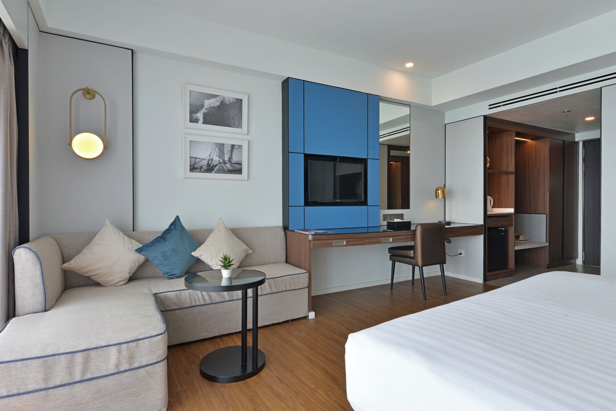 A modern hotel room with a bed, a sofa, a desk, and a small table.
