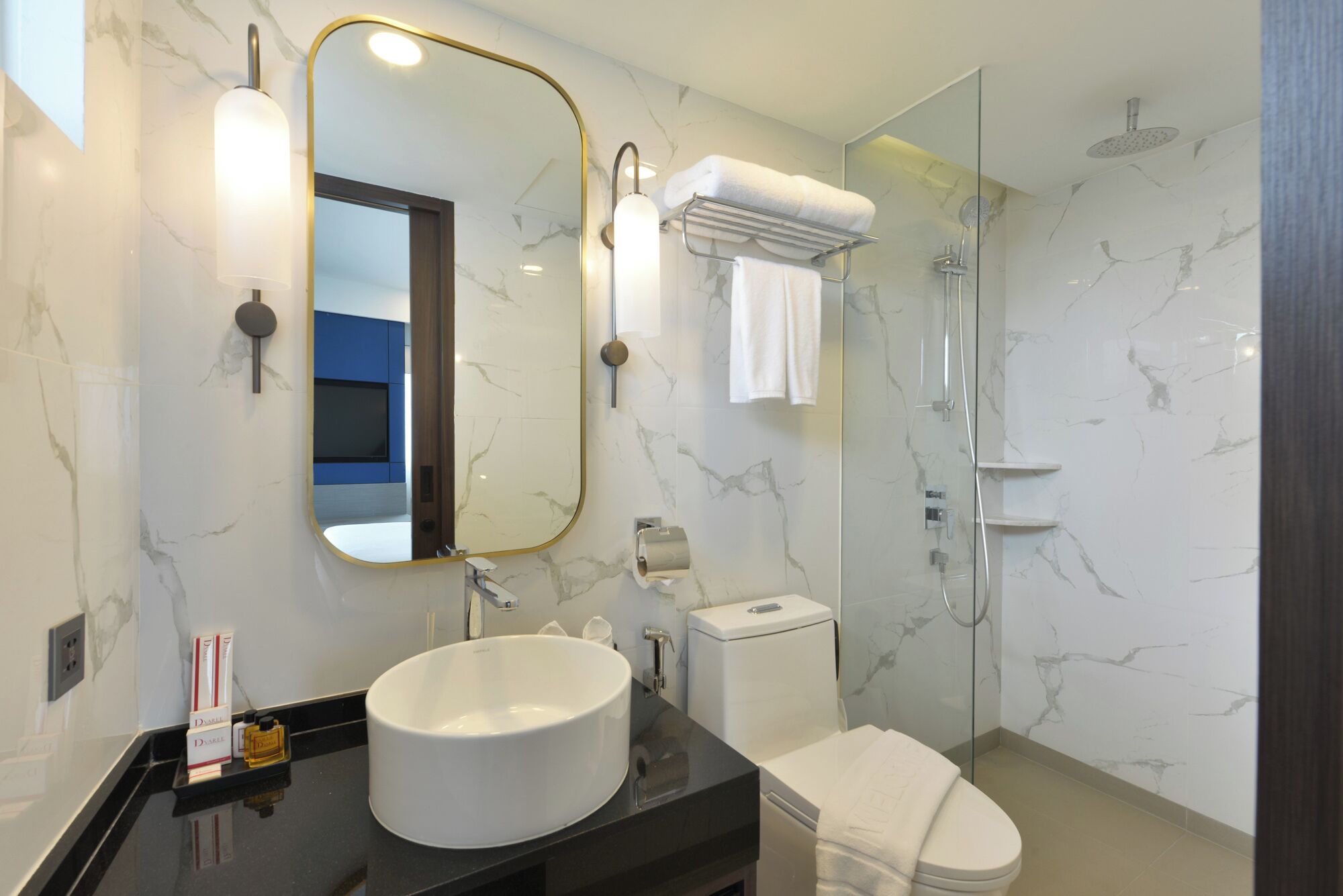 A modern bathroom with a marble backsplash, a round sink, a toilet, a glass shower enclosure, and a mirror with a gold frame.